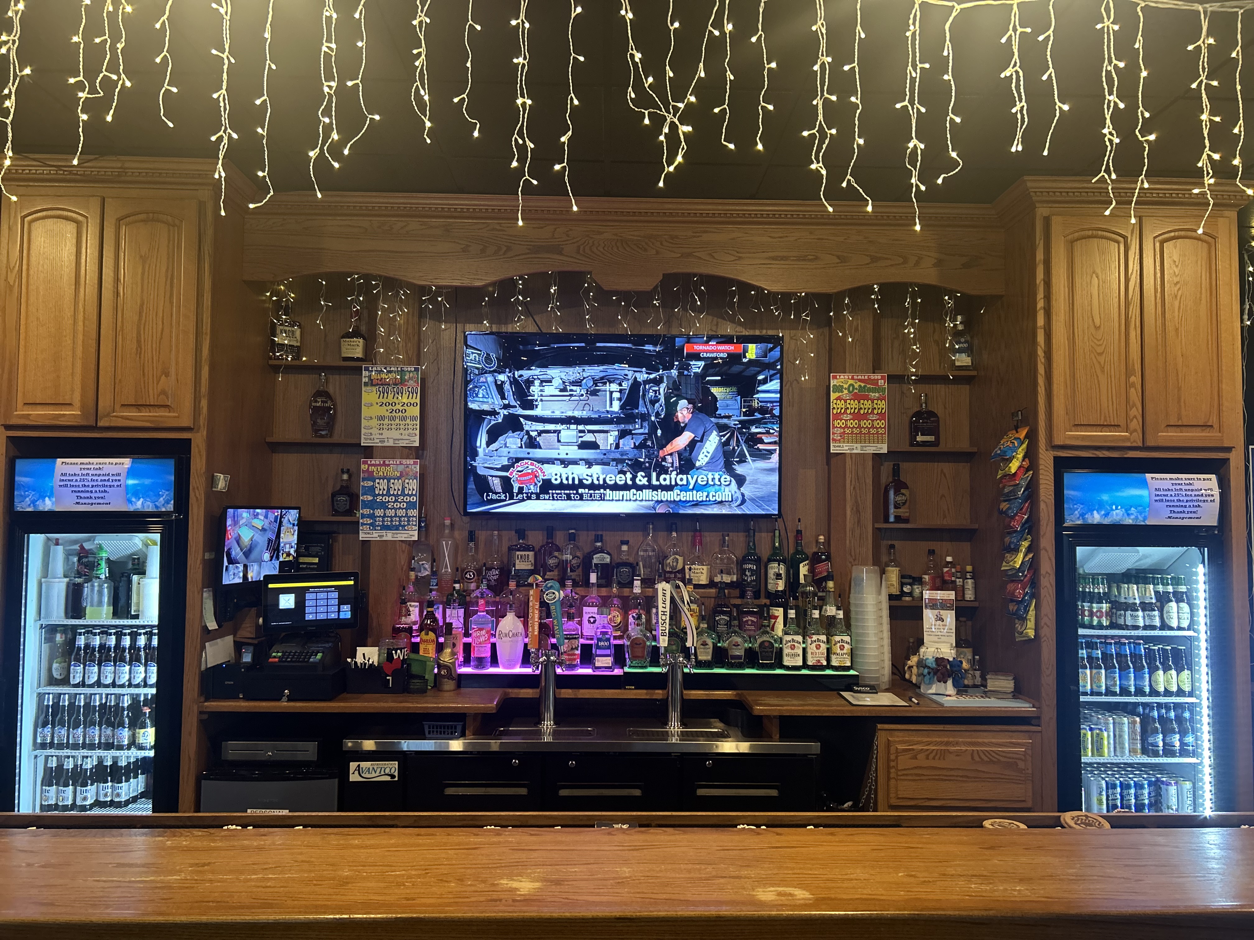 The Vault back bar — full liquor shelf, TV, string lights, and beer fridges