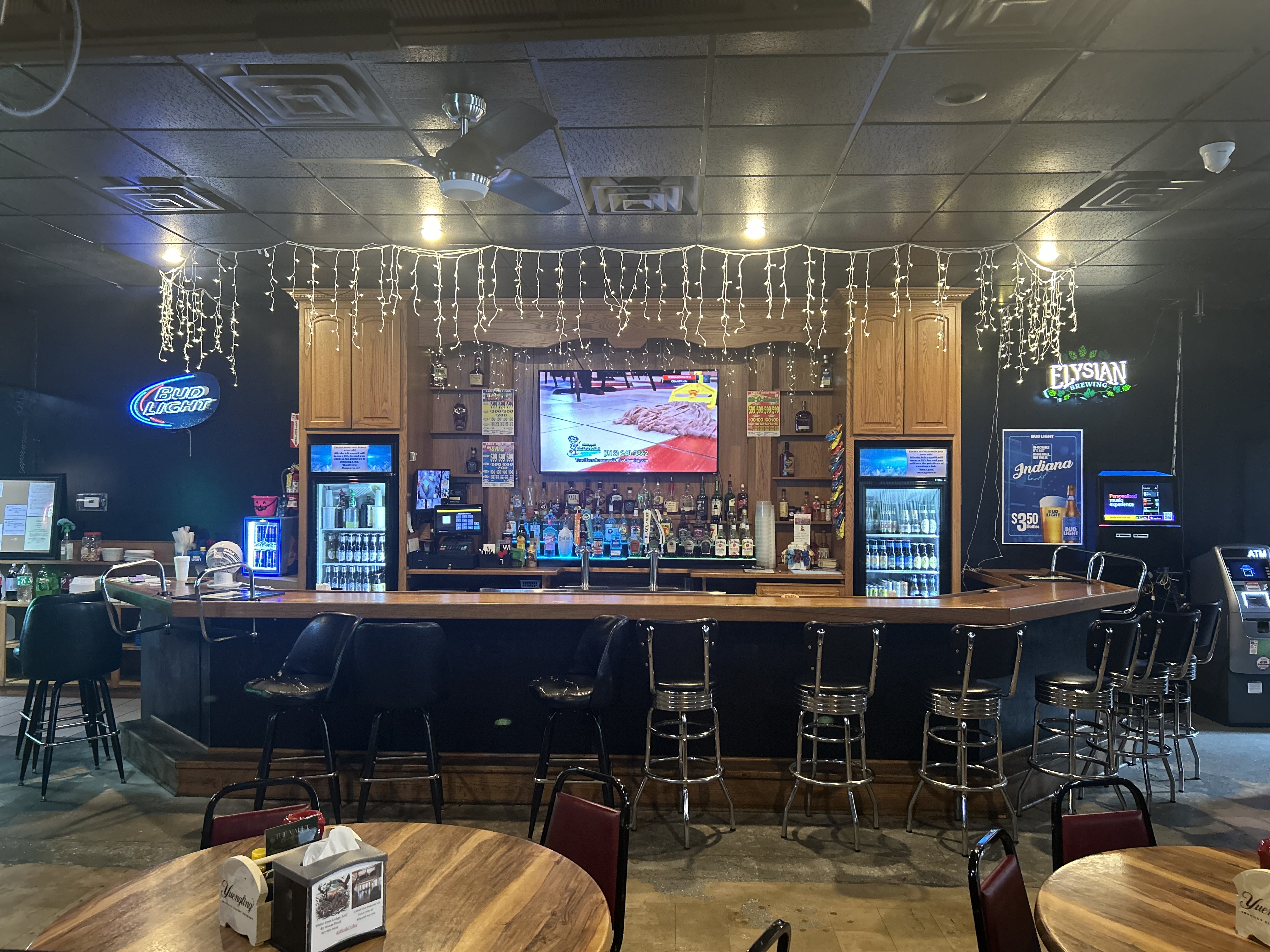The Vault bar — full overview with bar stools, back bar, string lights, and Coors Light sign